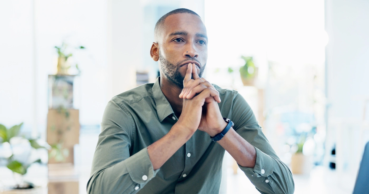 A man sitting in a bright room, hands together, thinking something through