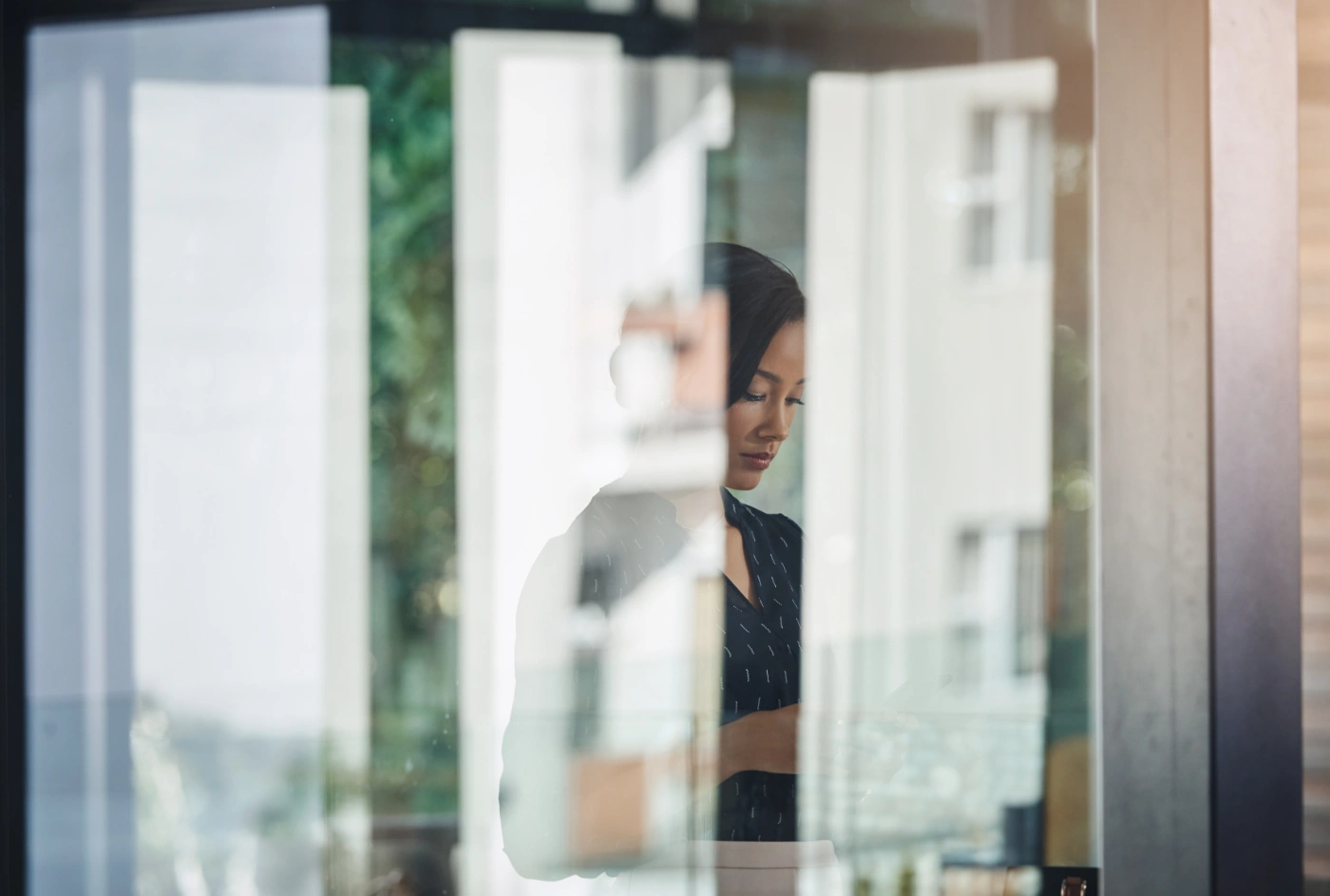 A woman standing at an office window, pausing to think