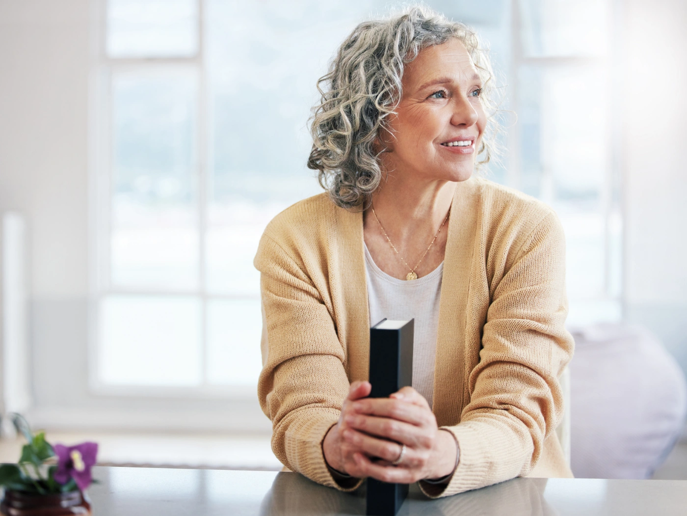 A woman sitting by a bright window at home, calm and at ease