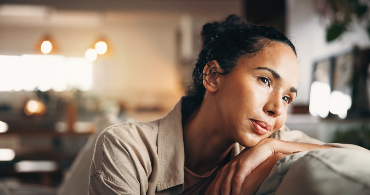 A woman sitting quietly at home, resting her chin on her hand, looking into the middle distance